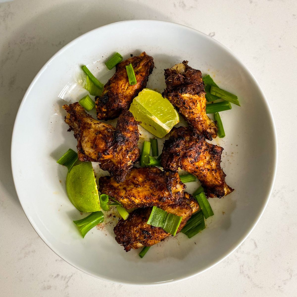 air fried jerk chicken wings in a white plate garnished with lime wedges and scallions