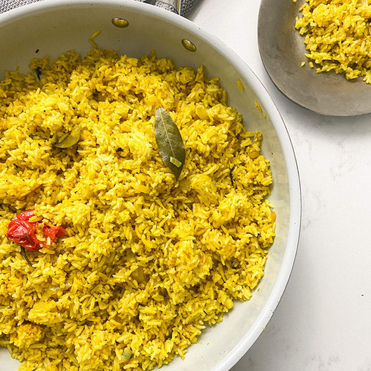 garlic turmeric rice in a large pan with a small plated version in the upper right hand corner