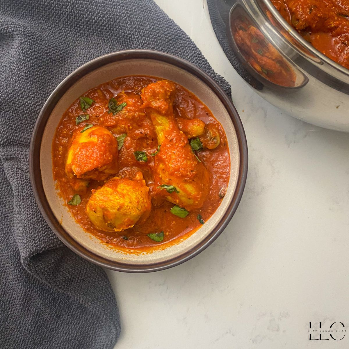 Nigerian chicken stew in a brown bowl with a pot of stew in the upper right hand corner