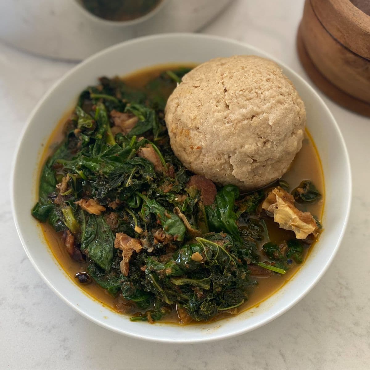 plated vegetable soup in a white bowl with fufu
